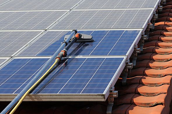 Nahaufnahme eines Dachs mit roten Ziegeln und Solarmodulen, auf den Modlen ein Reinigungsgerät