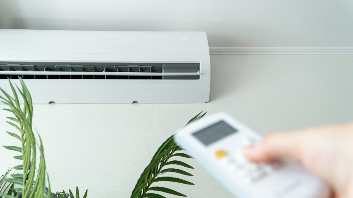 Klimaanlage an der Wand im Vordergrund Hand mit Remote Control