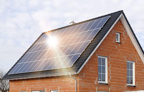 Rotes Backsteinhaus schräg seitlich mit Solarmodulen auf dem Dach, auf die die Sonne scheint